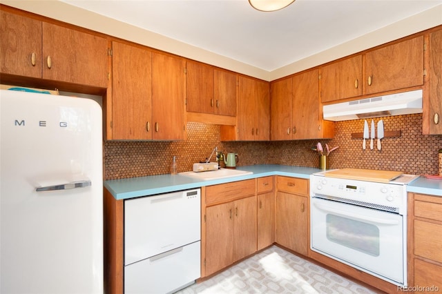 kitchen featuring white appliances, light countertops, under cabinet range hood, a sink, and backsplash