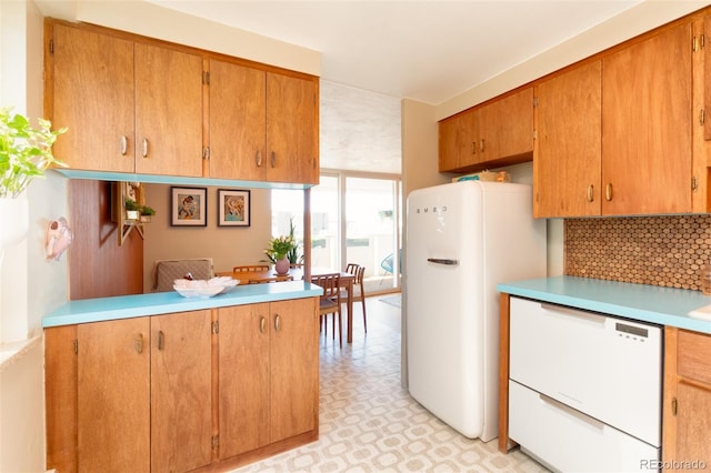 kitchen featuring white appliances, light countertops, a peninsula, decorative backsplash, and light floors