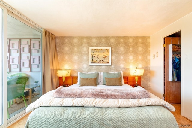 bedroom with wood finished floors, an accent wall, a spacious closet, and wallpapered walls