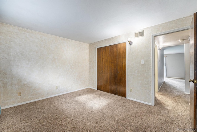 unfurnished bedroom with visible vents, a closet, a textured wall, baseboards, and carpet flooring