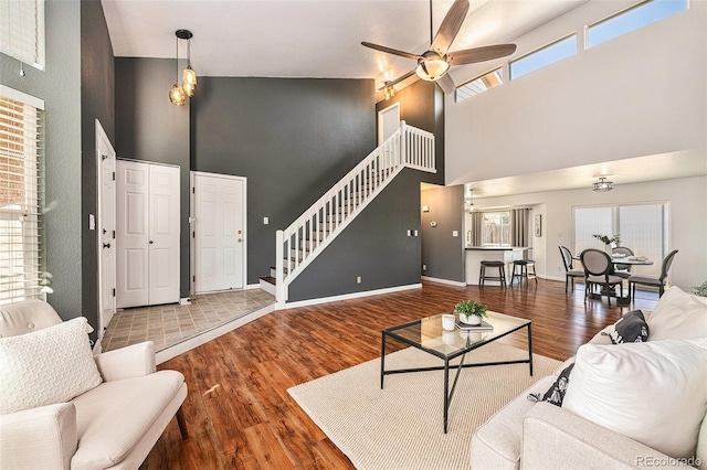 living room with ceiling fan, a healthy amount of sunlight, a towering ceiling, and hardwood / wood-style floors