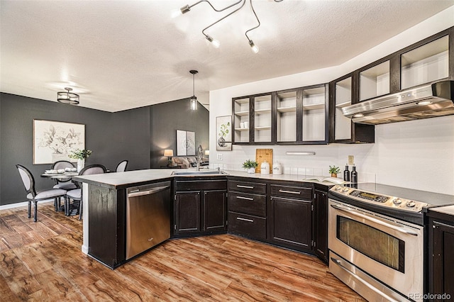 kitchen with wall chimney exhaust hood, stainless steel appliances, light hardwood / wood-style floors, sink, and hanging light fixtures