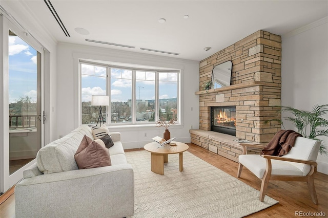 living area featuring ornamental molding, a stone fireplace, and wood finished floors