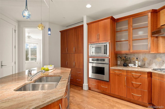 kitchen with tasteful backsplash, appliances with stainless steel finishes, brown cabinets, decorative light fixtures, and a sink