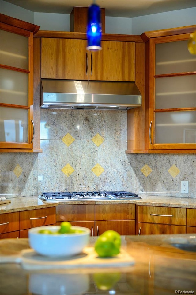 kitchen with brown cabinetry, glass insert cabinets, decorative backsplash, and extractor fan