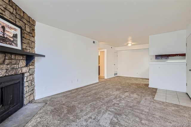 unfurnished living room featuring visible vents, baseboards, tile patterned floors, carpet, and a stone fireplace