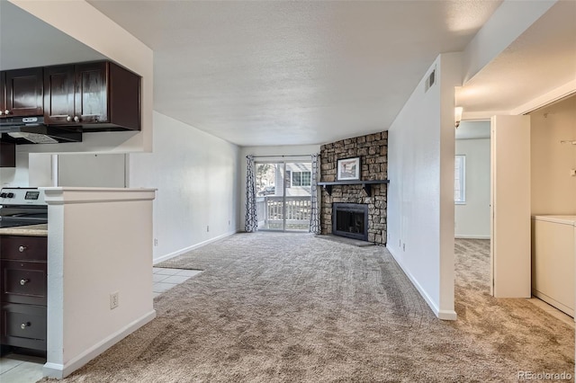 unfurnished living room featuring light carpet, washer / dryer, visible vents, a textured ceiling, and a stone fireplace