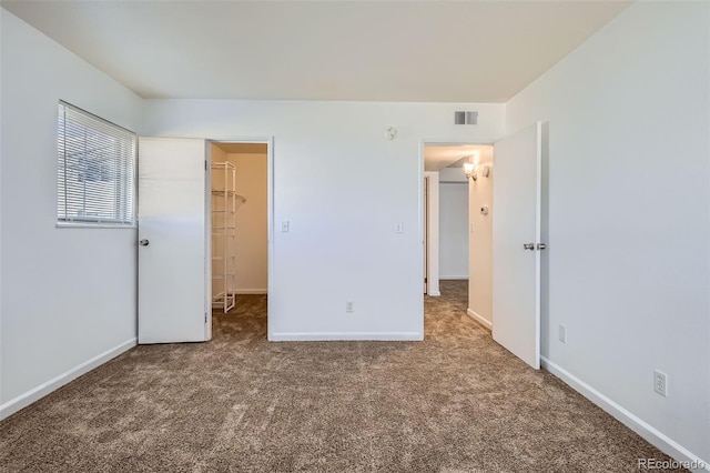 unfurnished bedroom with a spacious closet, carpet, visible vents, and baseboards