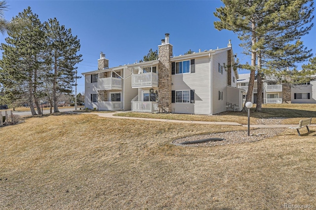 back of property featuring a chimney, a balcony, and a lawn