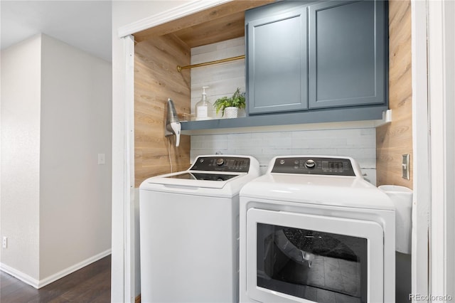 clothes washing area featuring dark wood-style flooring, washing machine and clothes dryer, cabinet space, wood walls, and baseboards