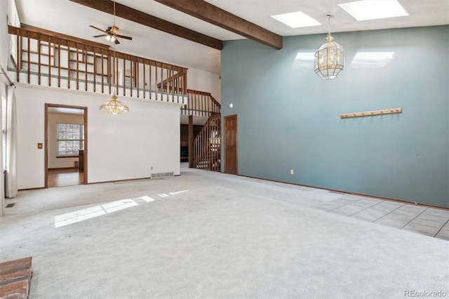 unfurnished living room featuring ceiling fan with notable chandelier, carpet flooring, a skylight, and beamed ceiling