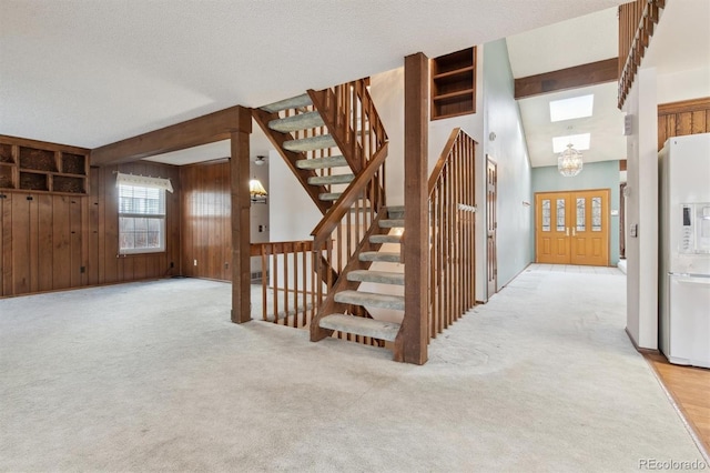 staircase with a textured ceiling, an inviting chandelier, wood walls, and carpet flooring