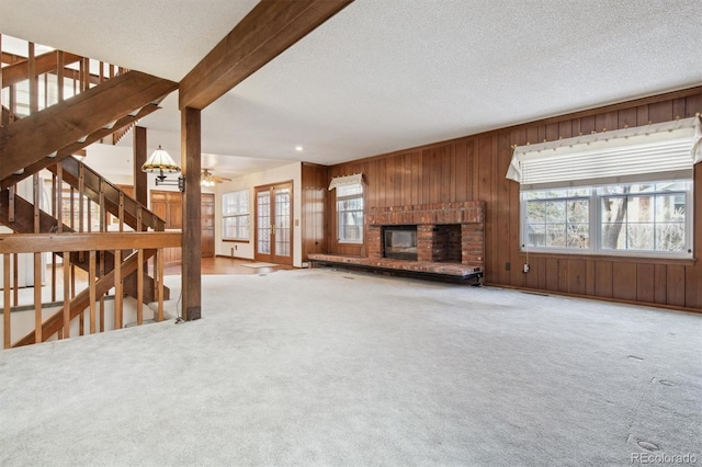 unfurnished living room featuring a brick fireplace, carpet floors, a textured ceiling, and beam ceiling