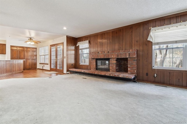 unfurnished living room featuring light carpet, a fireplace, ceiling fan, and a textured ceiling