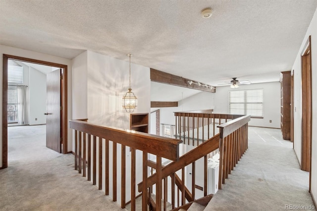 hall featuring a textured ceiling, light colored carpet, and an inviting chandelier