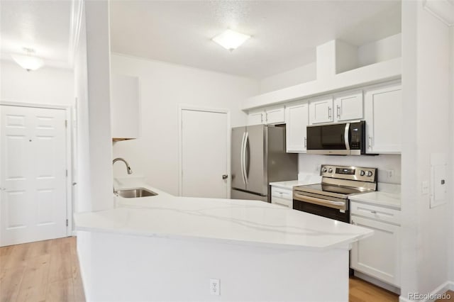 kitchen with a peninsula, light wood-style floors, white cabinets, a sink, and stainless steel appliances
