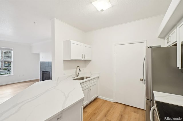 kitchen with light stone countertops, electric range oven, white cabinetry, a sink, and light wood finished floors