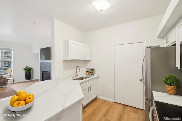 kitchen featuring light stone counters, a sink, light wood-style floors, a tiled fireplace, and white cabinetry