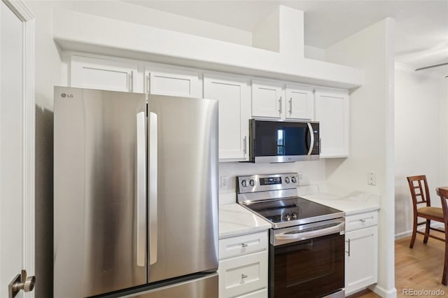 kitchen with light stone counters, light wood-style floors, appliances with stainless steel finishes, and white cabinets