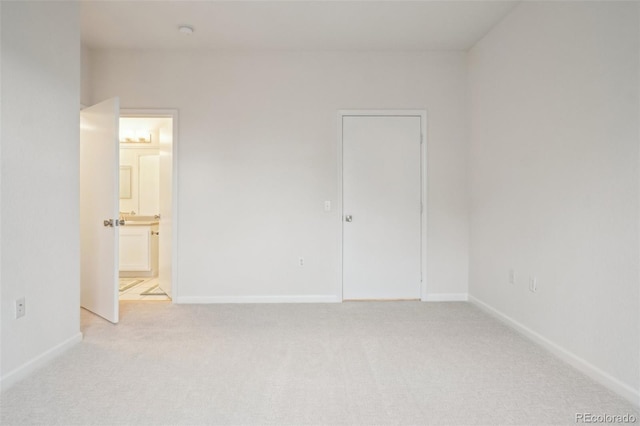 unfurnished bedroom featuring baseboards, connected bathroom, and light carpet