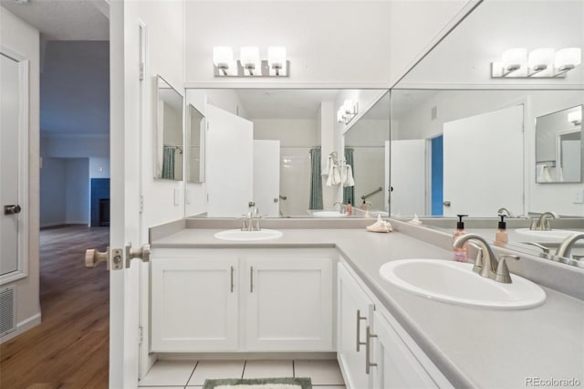 bathroom with a sink, double vanity, a shower stall, and wood finished floors