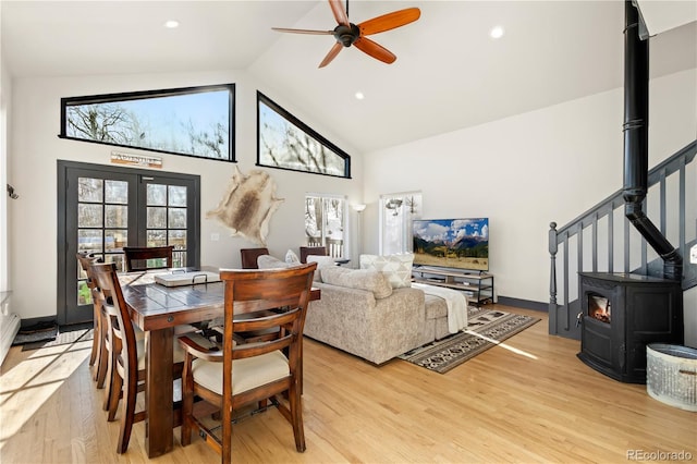 dining area with ceiling fan, high vaulted ceiling, light wood-type flooring, and a wood stove