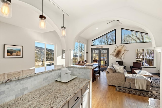 kitchen with hanging light fixtures, high vaulted ceiling, light stone countertops, light hardwood / wood-style floors, and french doors