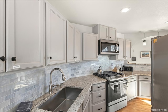 kitchen featuring sink, backsplash, stainless steel appliances, light hardwood / wood-style floors, and decorative light fixtures