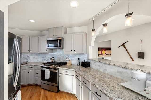 kitchen featuring hanging light fixtures, tasteful backsplash, appliances with stainless steel finishes, and light wood-type flooring