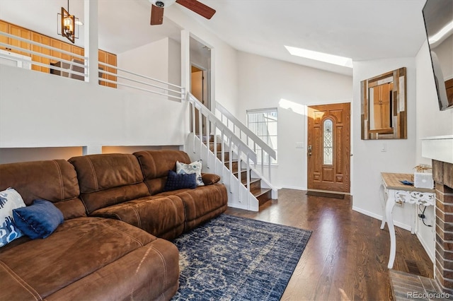 living room with baseboards, stairway, vaulted ceiling with skylight, wood finished floors, and a ceiling fan