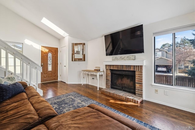 living area featuring vaulted ceiling with skylight, a brick fireplace, wood finished floors, and baseboards