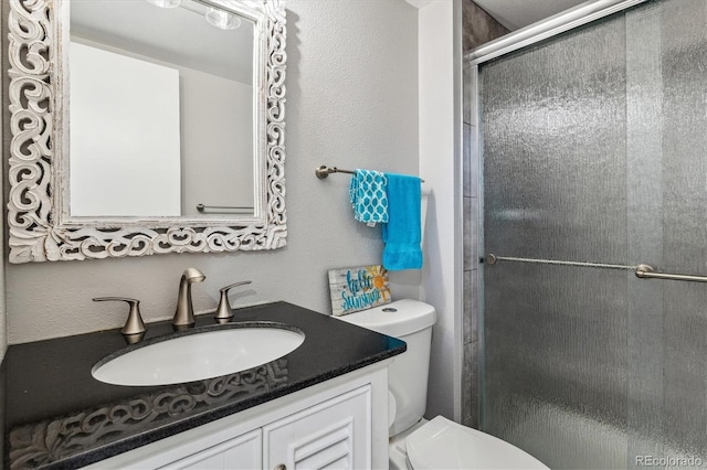 full bath with toilet, a stall shower, vanity, and a textured wall