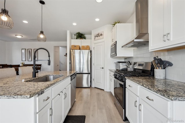 kitchen featuring pendant lighting, appliances with stainless steel finishes, white cabinets, a sink, and wall chimney range hood