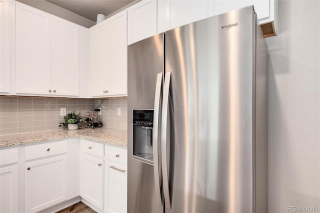 kitchen with decorative backsplash, stainless steel fridge, light stone countertops, and white cabinets