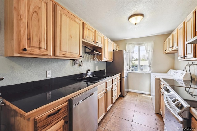 kitchen with tile countertops, a textured ceiling, appliances with stainless steel finishes, a sink, and separate washer and dryer