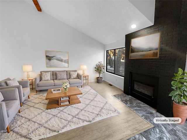 living room featuring lofted ceiling, a textured ceiling, light wood-type flooring, and a brick fireplace