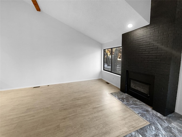 living room with hardwood / wood-style flooring, vaulted ceiling, a brick fireplace, and a textured ceiling