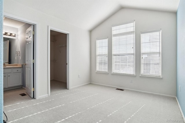 unfurnished bedroom with lofted ceiling, connected bathroom, light carpet, a walk in closet, and a closet