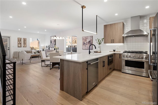 kitchen with premium appliances, kitchen peninsula, light hardwood / wood-style floors, wall chimney exhaust hood, and sink