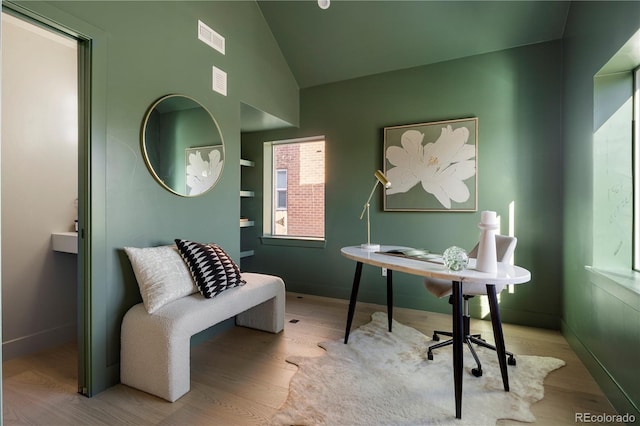 home office featuring built in shelves, vaulted ceiling, and light hardwood / wood-style floors