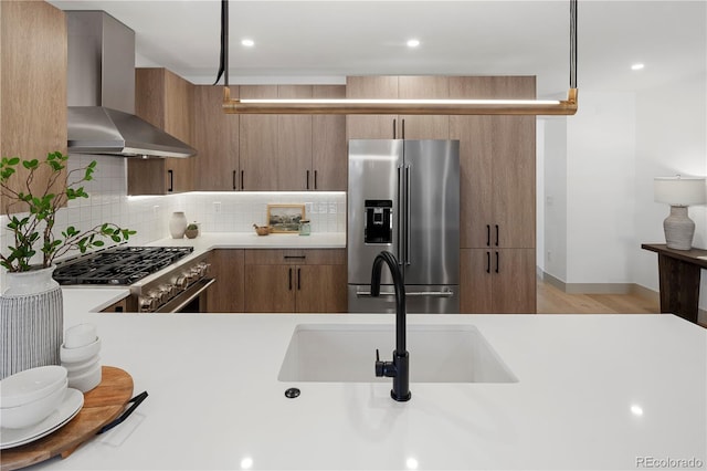 kitchen with pendant lighting, premium appliances, wall chimney range hood, sink, and backsplash