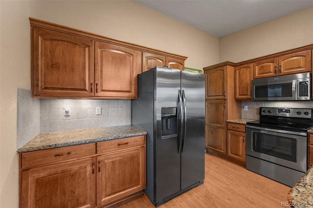 kitchen with light stone counters, light wood-type flooring, brown cabinets, and stainless steel appliances