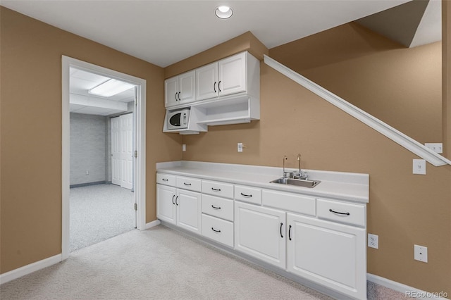 kitchen featuring white cabinetry, baseboards, light carpet, and a sink