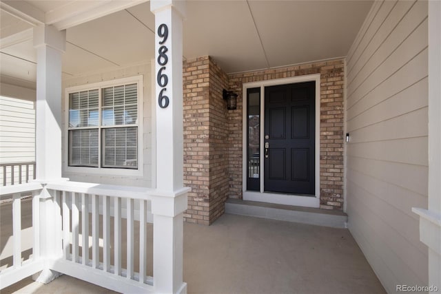 doorway to property featuring brick siding and a porch