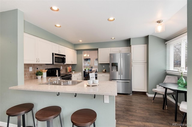 kitchen with dark wood finished floors, a peninsula, white cabinets, appliances with stainless steel finishes, and tasteful backsplash