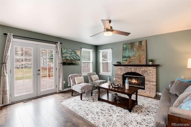 living area featuring visible vents, a brick fireplace, french doors, wood finished floors, and a ceiling fan