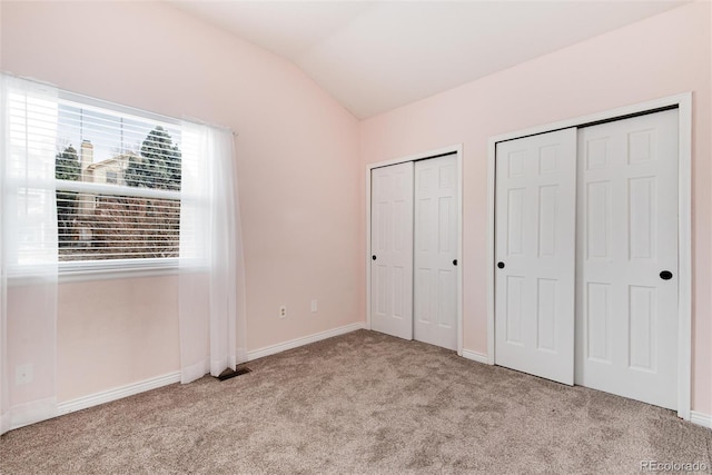 unfurnished bedroom with lofted ceiling, baseboards, multiple closets, and carpet floors