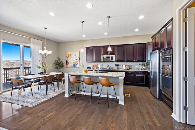 kitchen with dark brown cabinets, a kitchen bar, appliances with stainless steel finishes, dark wood-style floors, and a kitchen island with sink