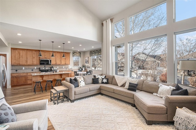 living area with a towering ceiling, light wood-style floors, and recessed lighting