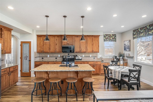 kitchen with arched walkways, brown cabinetry, a sink, and a kitchen island with sink